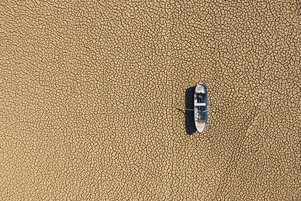 Aerial view of fisher boat on dried, cracked seabed in drought