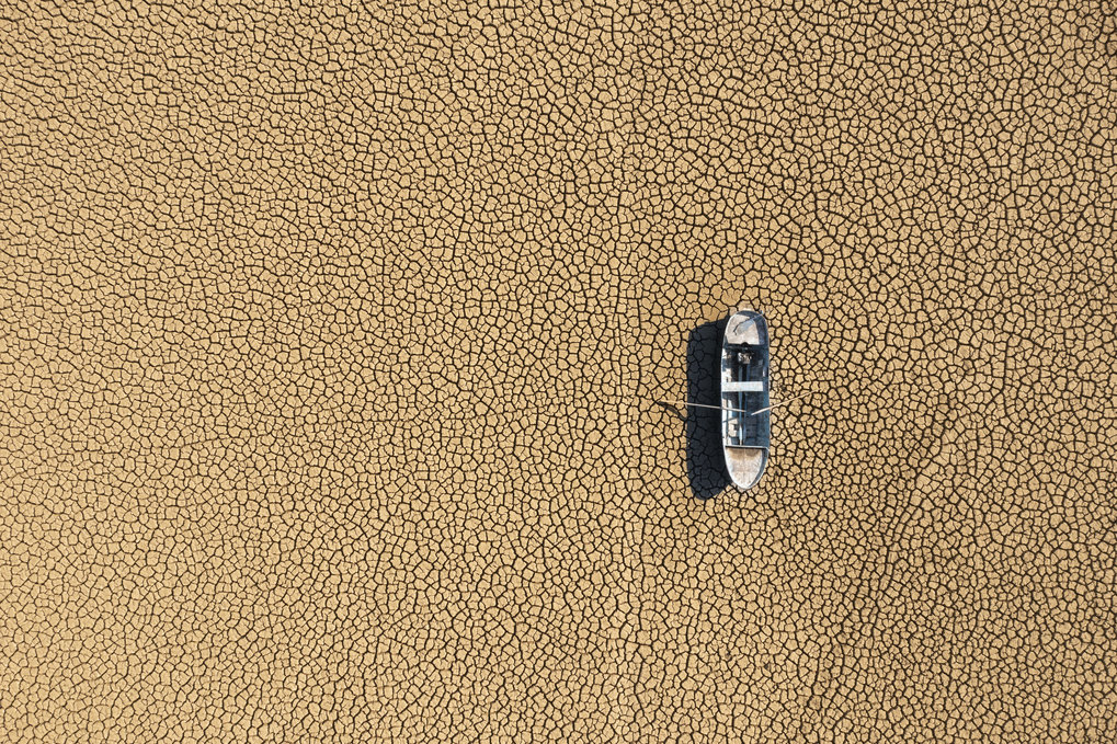 Aerial view of a single fishing boat on the dry surface of a drought lake bed. 